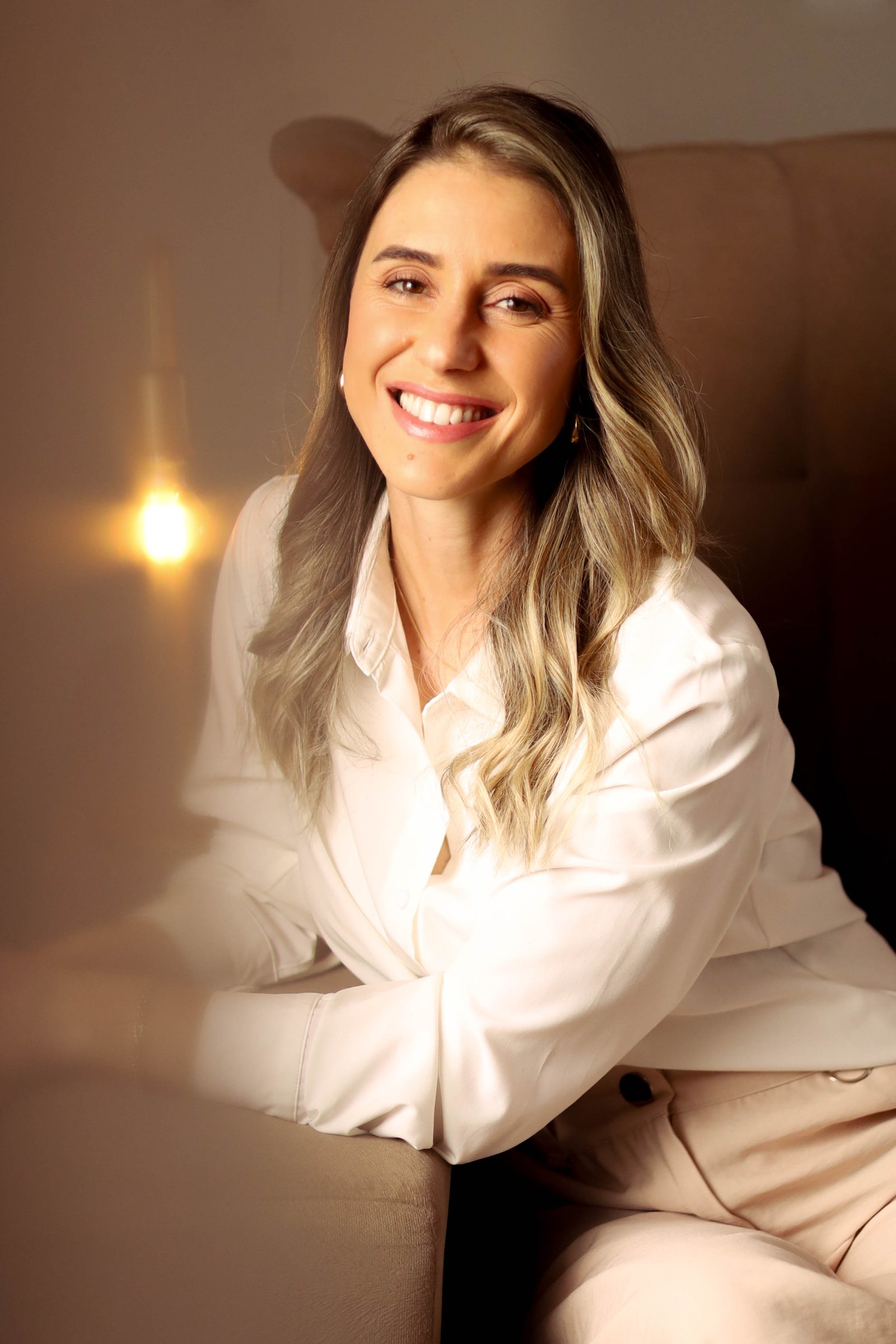 Pâmela no sofá, camisa branca, acolhedora.